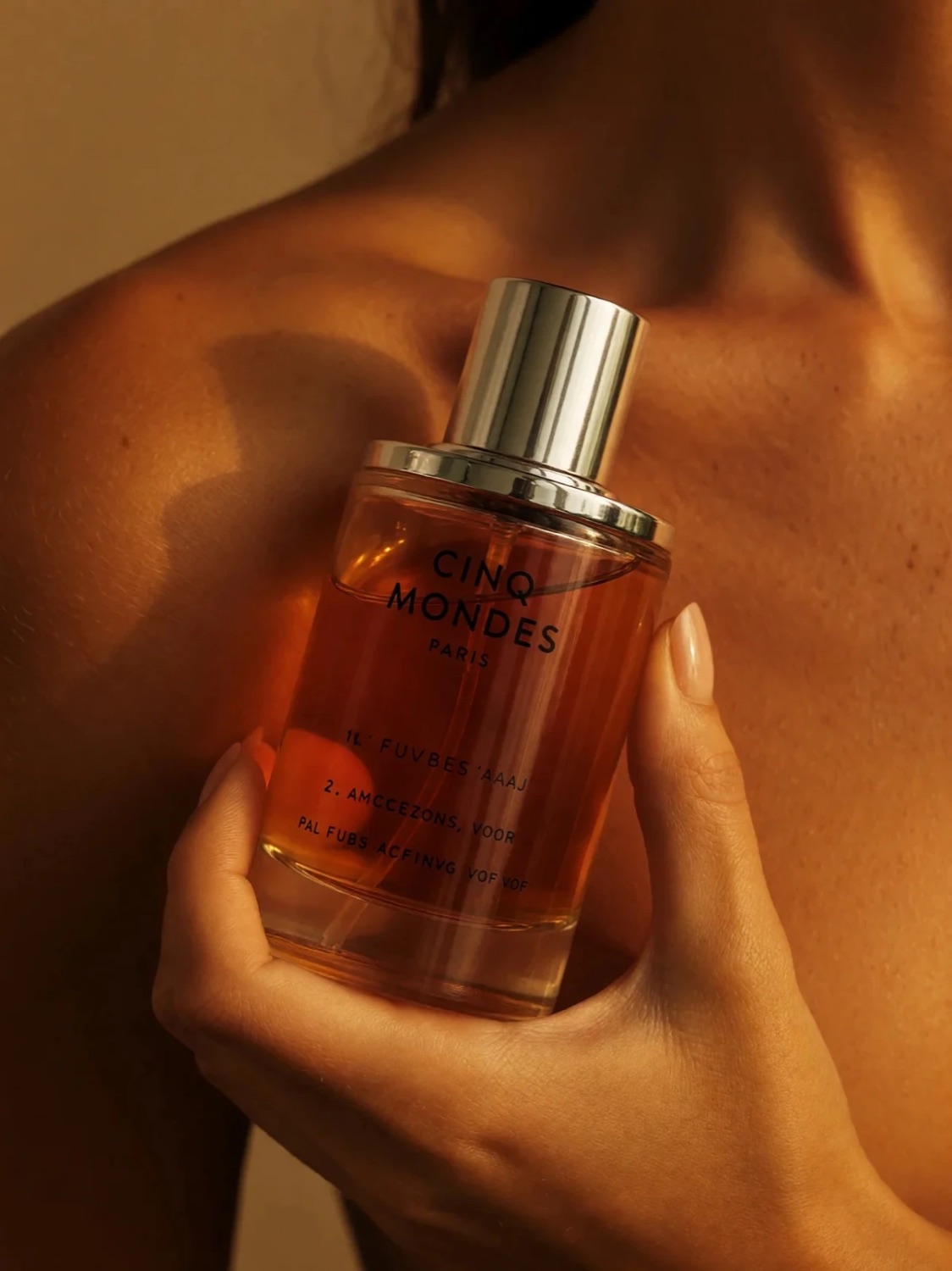 CINQ MONDES fragrance product photography — bottle against skin in warm light